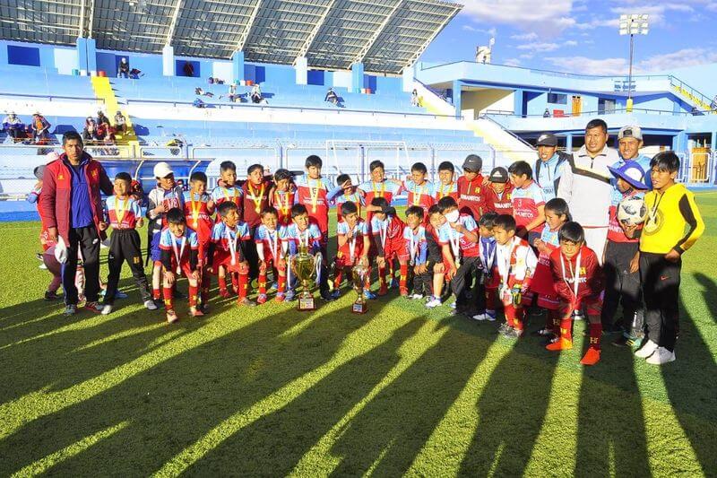 En primera plana la Escuela de Fútbol Hermanitos y un niño portando un trofeo.