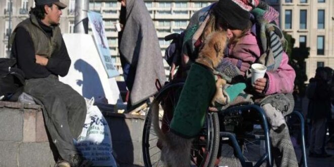 Una mujer sin hogar juega con un perro mientras toma un desayuno caliente gratis en la Plaza de la República en Buenos Aires.