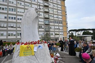 Fieles rezan ante la estatua de Juan Pablo II en el exterior del Hospital Gemelli, donde se encuentra internado el Papa Francisco. Foto AFP